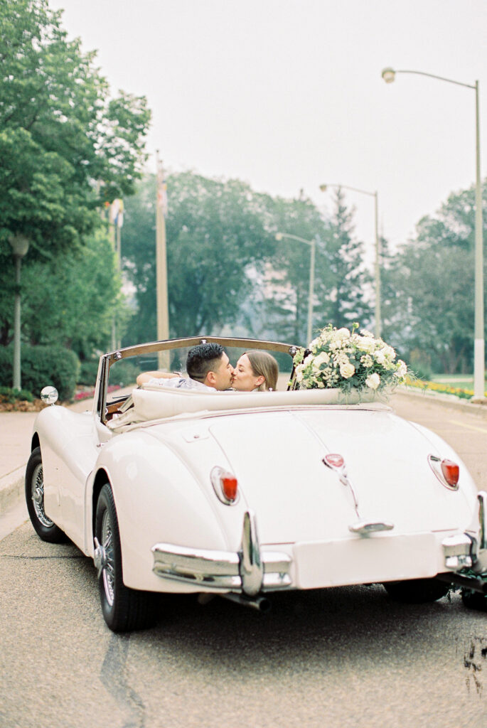 bride and groom kissing in the back of a vintage jaguar